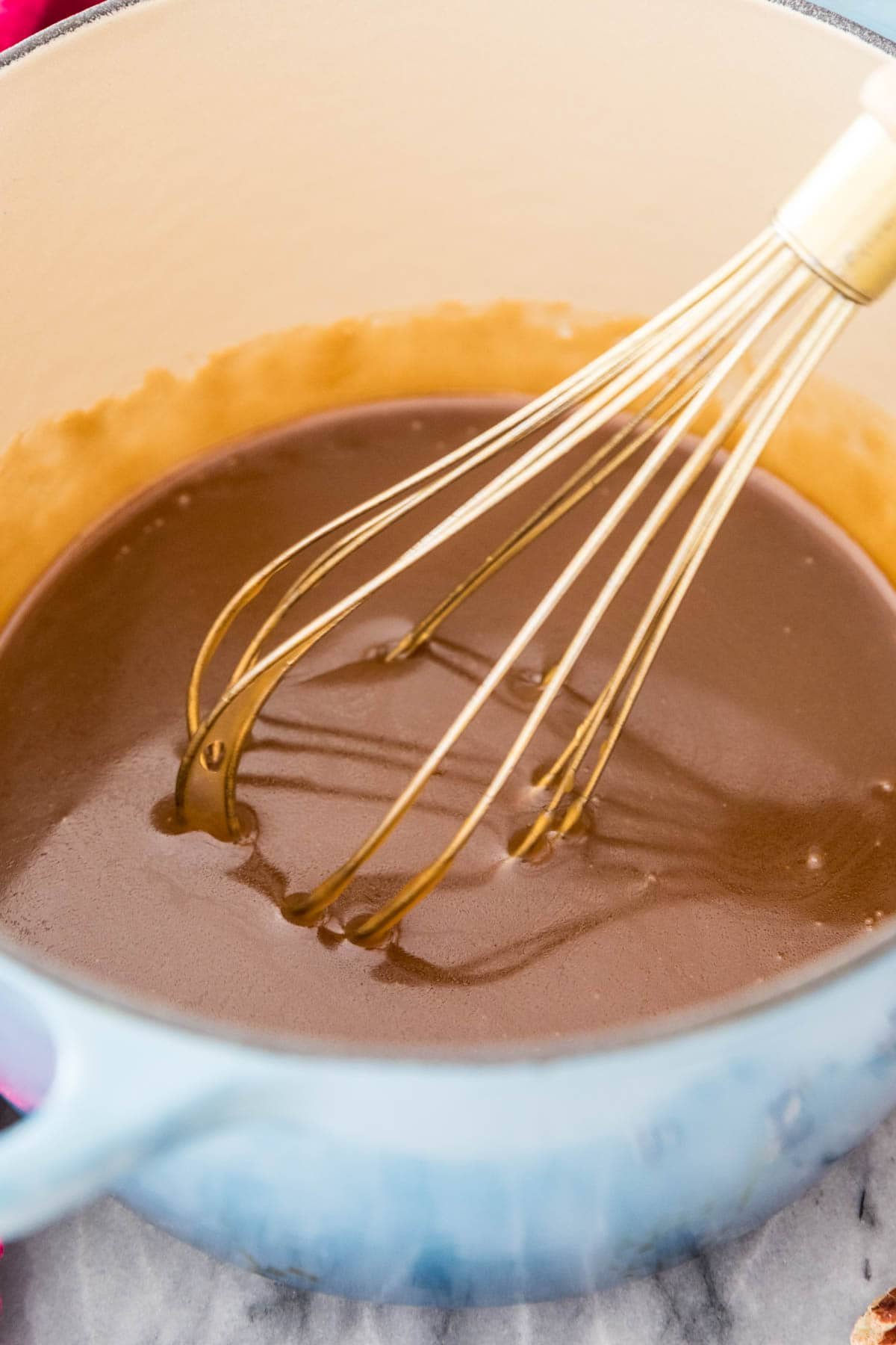 Sticky bun glaze, dark caramel-colored in blue saucepan with gold whisk.