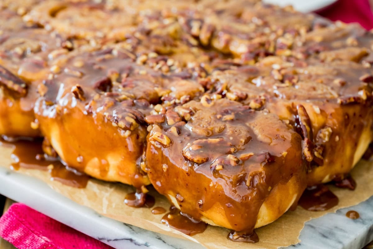 Sticky buns dripping glaze onto parchment paper on marble board.