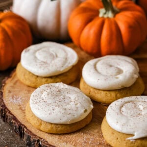 4 Pumpkin Cookies with Cream Cheese Frosting, orange pumpkins in the background.