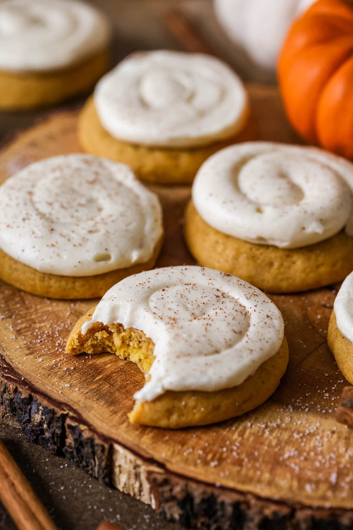 Pumpkin cookies with cream cheese frosting, a bite missing from the cookie in the foreground showing soft interior.