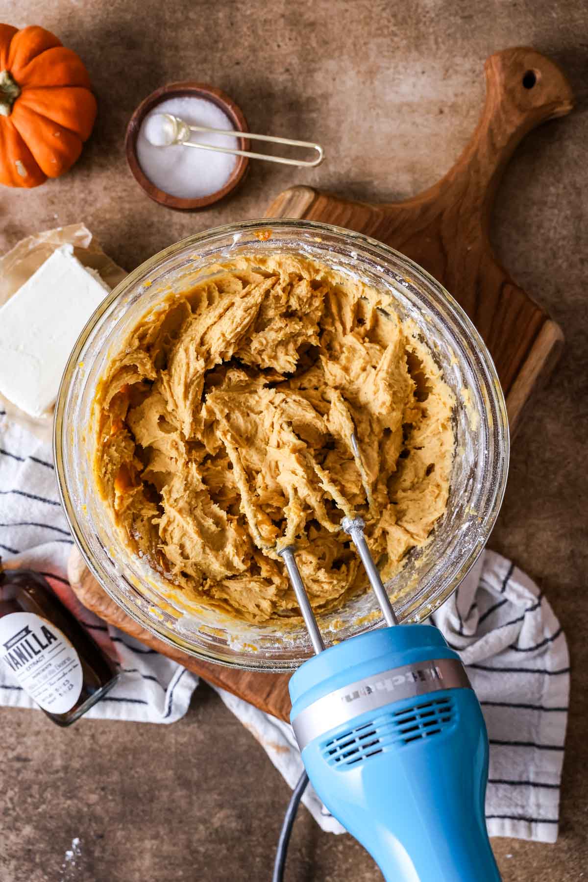 Pumpkin cookie cookie dough in a glass mixing bowl with blue mixer.