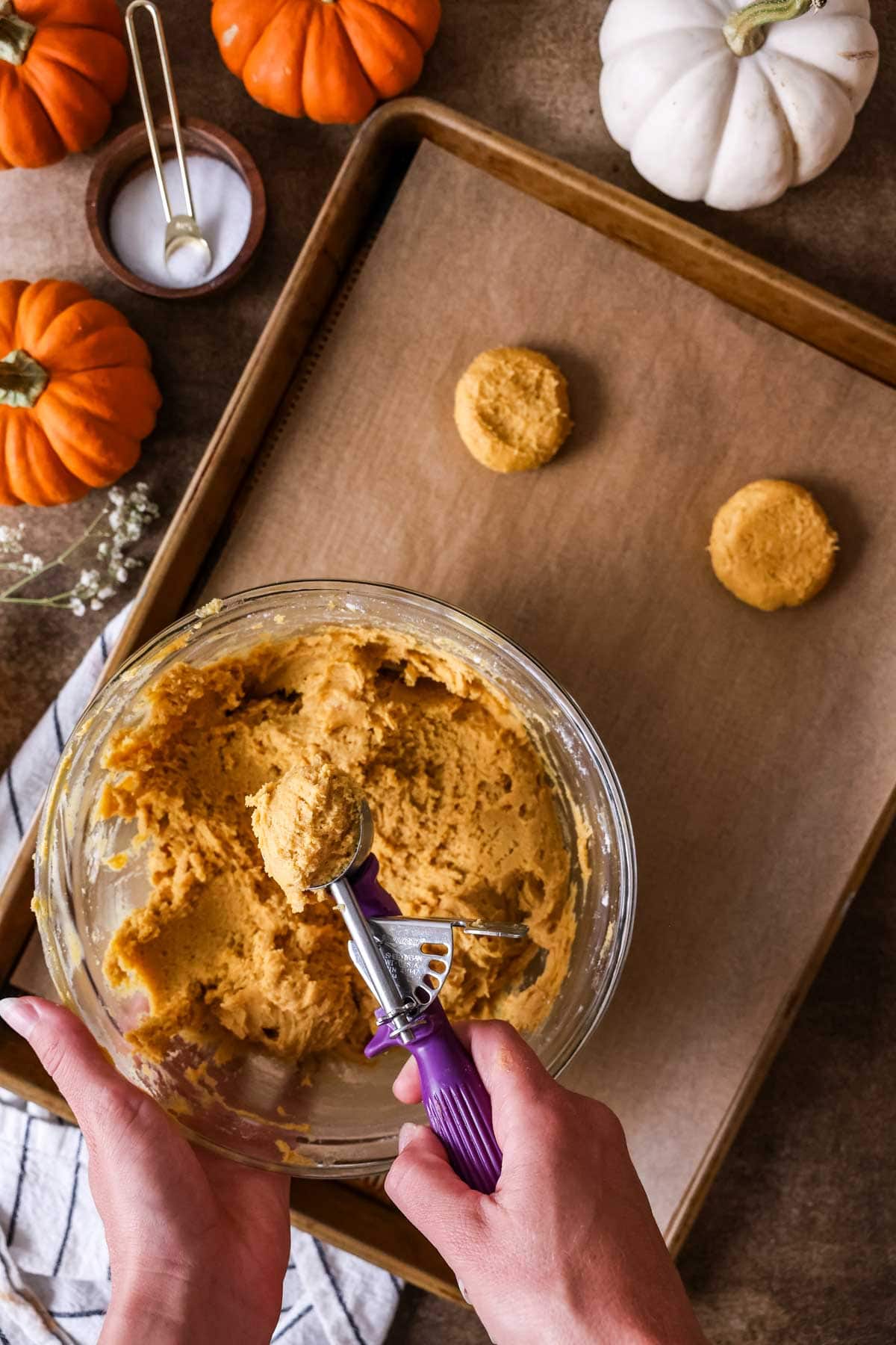 Scooping pumpkin cookie dough onto a parchment paper lined baking sheet.