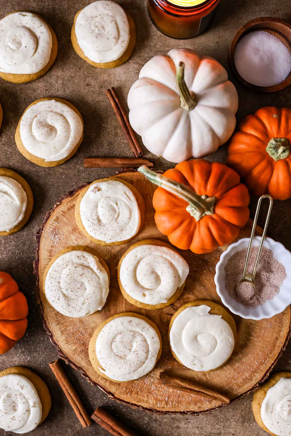 Overhead view of frosted pumpkin cookies with cream cheese frosting, surrounded by small pumpkins.