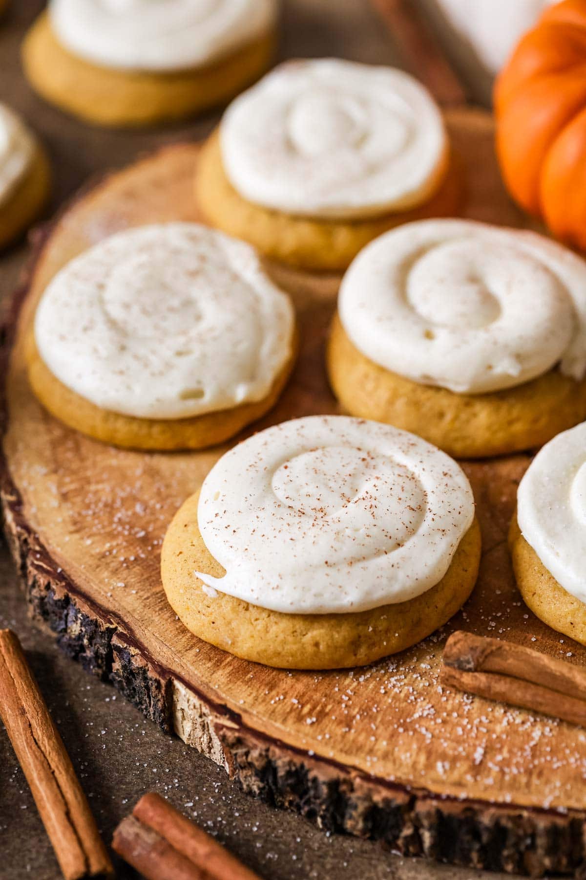 Four pumpkin cookies with cream cheese frosting, orange pumpkins in the background.